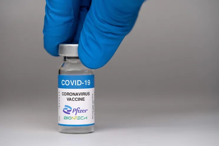 Vacuna Pfizer contra el virus Covid-19. La mano del médico toma un frasco de vacuna contra el coronavirus sobre un fondo blanco.