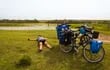 Una cicloturista descansa al aire libre, luego de una jornada de pedaleo. A su lado, su bici y la de su acompañante, cargadas con alforjas con todo lo necesario para seguir viajando.