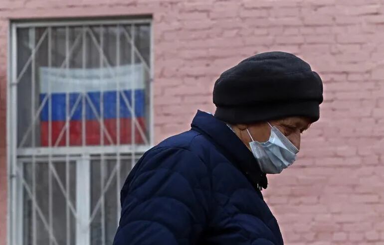 Una mujer protegida por mascarilla camina por una calle de Moscú.