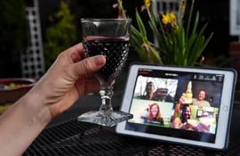 Una mujer levanta su copa y brinda con sus amigos durante una "happy hour" virtual.