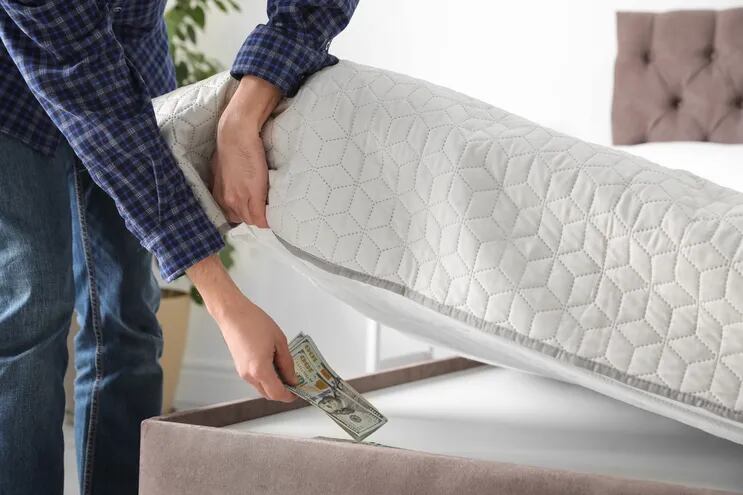 Un hombre esconde billetes de dólar bajo un colchón.