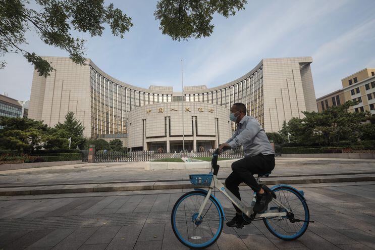 Un hombre pedalea su bicicleta frente a la sede del Banco Popular de China, en Pekín, China.