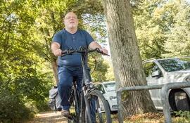 Un hombre barrigón de unos sesenta años pasea en bicicleta al aire libre.