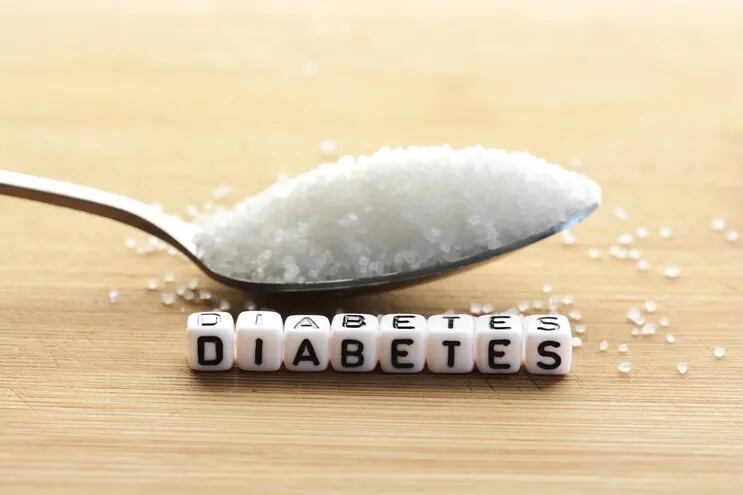 Una cuchara sopera cargada de azúcar y dados que forman la palabra "Diabetes" sobre una mesa