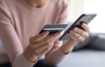 Una mujer revisa su tarjeta de crédito para realizar compras en línea en su teléfono celular.