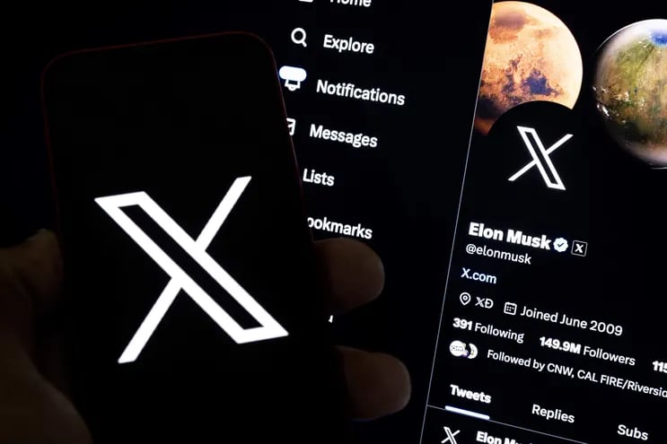 Un usuario sostiene un teléfono móvil que muestra el logotipo 'X' frente a una pantalla que muestra el perfil en esa misma red social de Elon Musk, en Los Ángeles, California (EE.UU.).