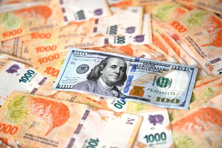 Imagen ilustrativa: un billete de 100 dólares y billetes de 1.000 pesos argentinos.